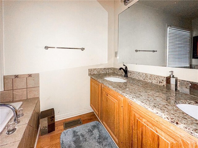 bathroom with tiled tub, hardwood / wood-style floors, and vanity