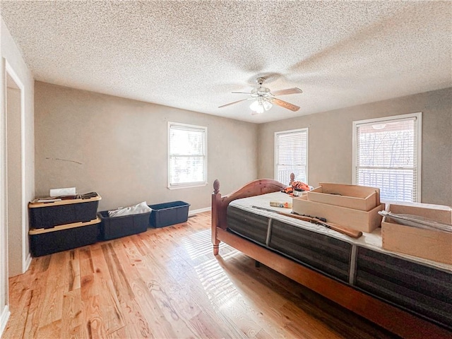 bedroom featuring multiple windows, a textured ceiling, light hardwood / wood-style floors, and ceiling fan