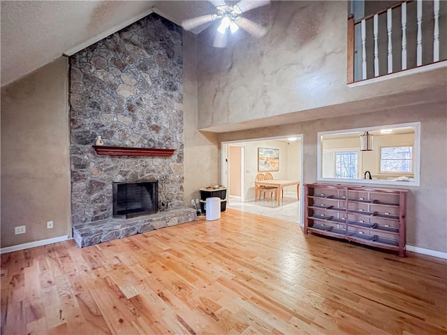 unfurnished living room with ceiling fan, a stone fireplace, wood-type flooring, and high vaulted ceiling