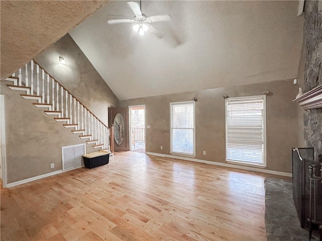 unfurnished living room featuring ceiling fan, a stone fireplace, light wood-type flooring, and high vaulted ceiling