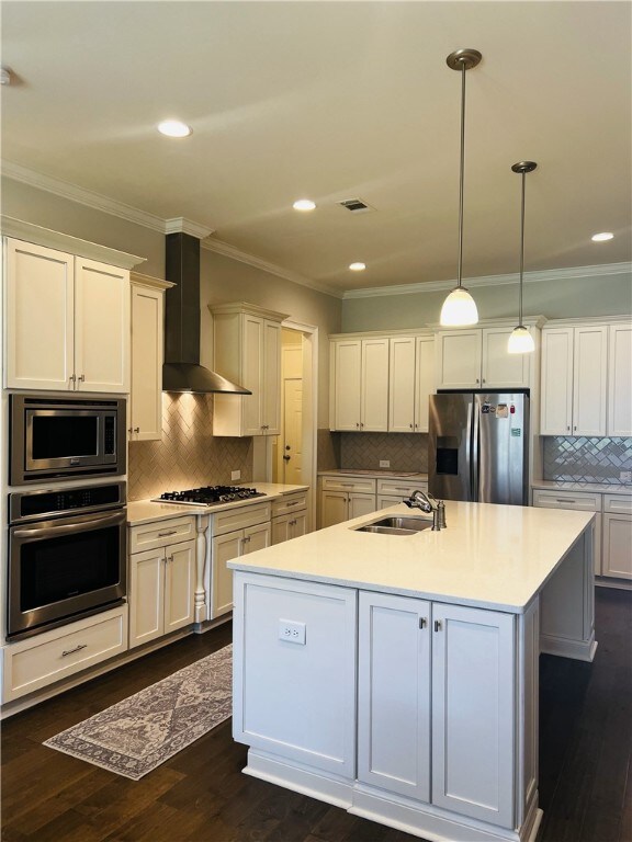 kitchen with pendant lighting, backsplash, a center island with sink, wall chimney range hood, and appliances with stainless steel finishes