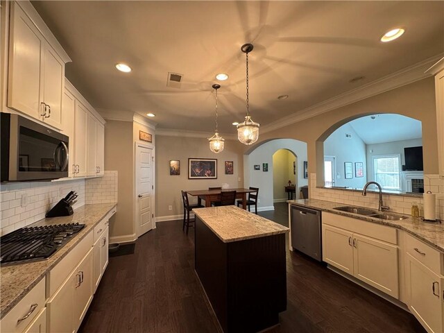 kitchen with ornamental molding, stainless steel appliances, dark wood finished floors, a sink, and arched walkways