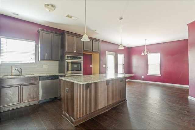 kitchen with light stone counters, backsplash, appliances with stainless steel finishes, dark wood-type flooring, and a sink