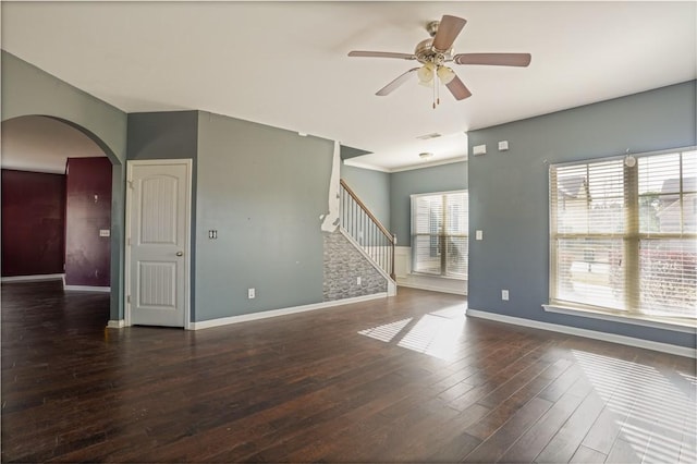 empty room with baseboards, stairs, arched walkways, and wood finished floors