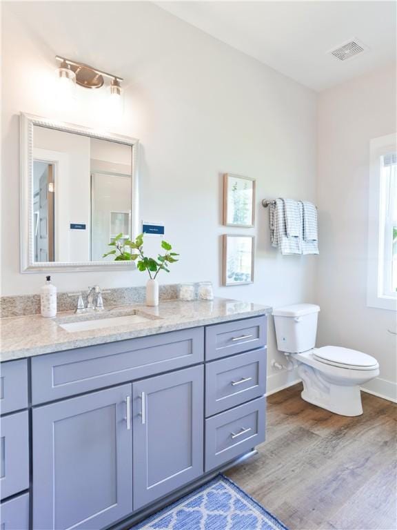 bathroom featuring visible vents, baseboards, toilet, wood finished floors, and vanity