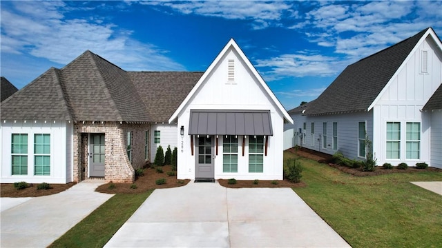 modern farmhouse featuring a standing seam roof, board and batten siding, a front lawn, and a shingled roof