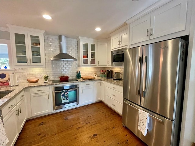 kitchen with appliances with stainless steel finishes, backsplash, white cabinets, and wall chimney range hood