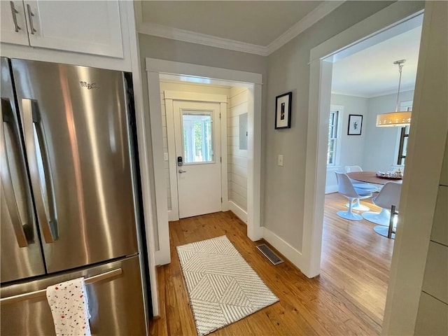 doorway to outside featuring light wood finished floors, baseboards, visible vents, and crown molding