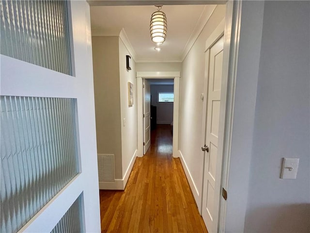 hall featuring ornamental molding, visible vents, baseboards, and wood finished floors