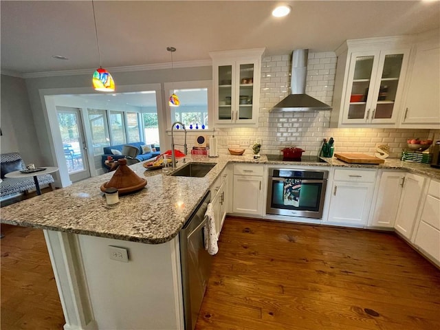 kitchen featuring wall chimney exhaust hood, appliances with stainless steel finishes, ornamental molding, a peninsula, and a sink