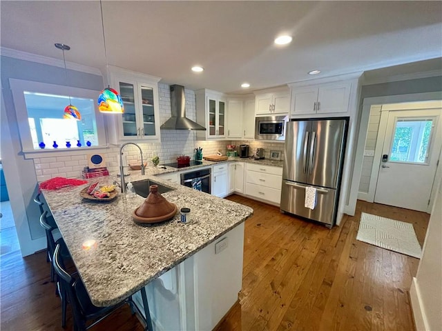 kitchen featuring dark wood finished floors, stainless steel appliances, a sink, wall chimney range hood, and a peninsula