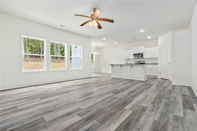 unfurnished living room featuring ceiling fan with notable chandelier, light hardwood / wood-style floors, sink, and a wealth of natural light