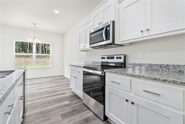 kitchen featuring light stone counters, white cabinets, stainless steel appliances, and a notable chandelier