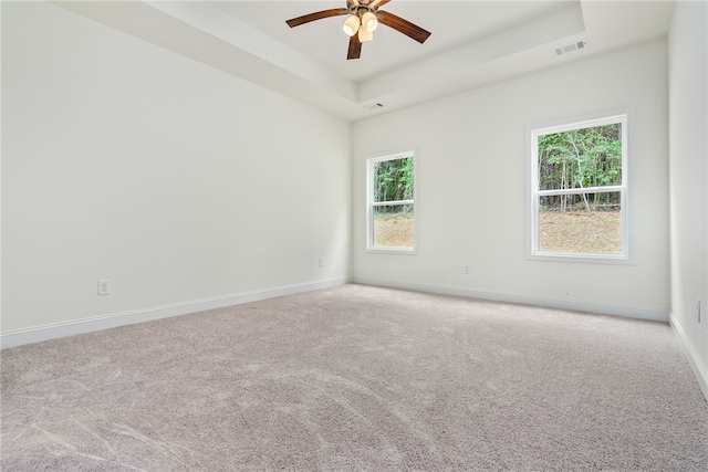 carpeted empty room with a tray ceiling, a wealth of natural light, and ceiling fan