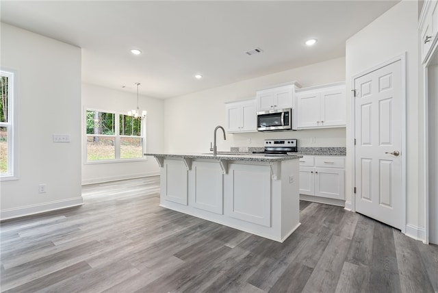 kitchen with white cabinetry, light stone countertops, hanging light fixtures, a kitchen island with sink, and appliances with stainless steel finishes