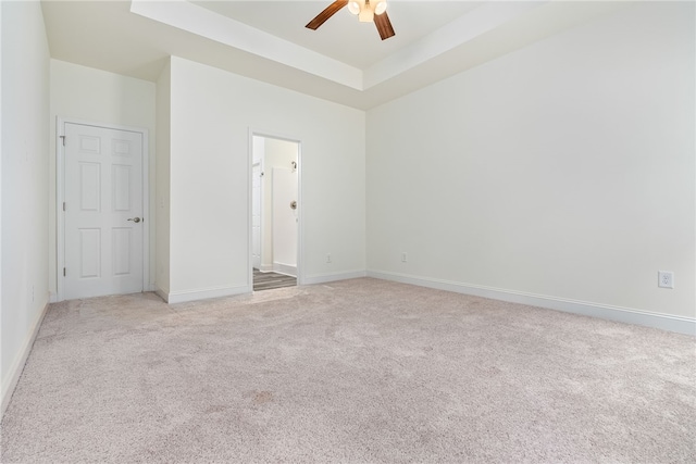 interior space with ensuite bathroom, a raised ceiling, ceiling fan, and light colored carpet