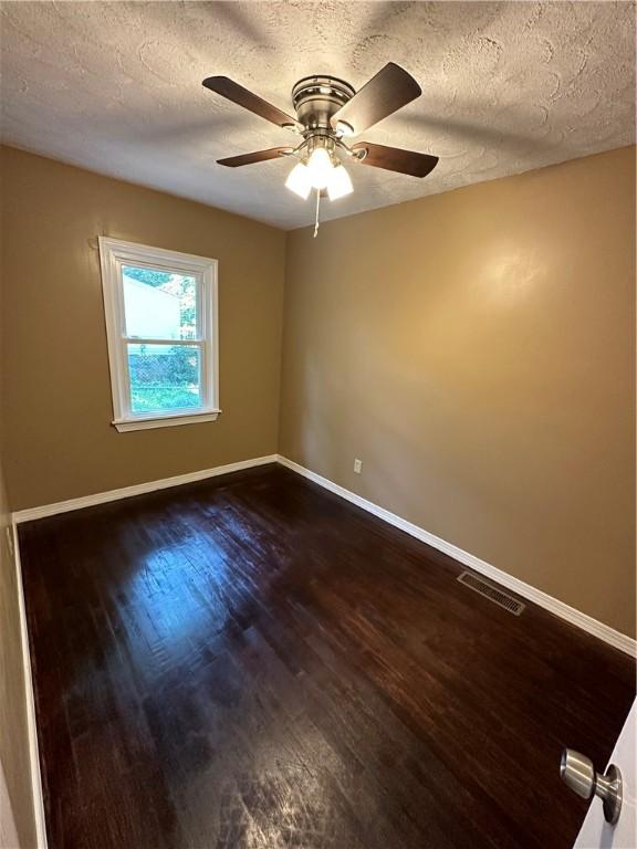 empty room with ceiling fan, dark hardwood / wood-style flooring, and a textured ceiling