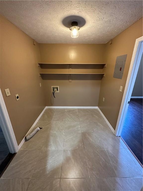 clothes washing area featuring electric panel, hookup for a washing machine, a textured ceiling, and hookup for an electric dryer