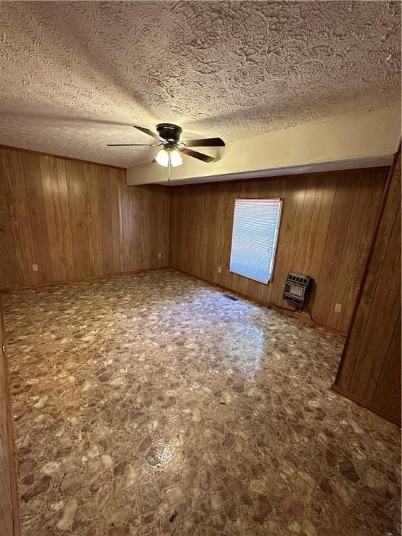 unfurnished room with ceiling fan, wood walls, a textured ceiling, and heating unit