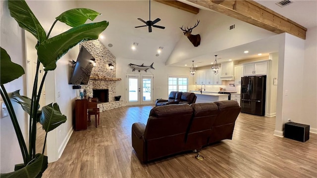 living room with beamed ceiling, high vaulted ceiling, a fireplace, and light hardwood / wood-style floors