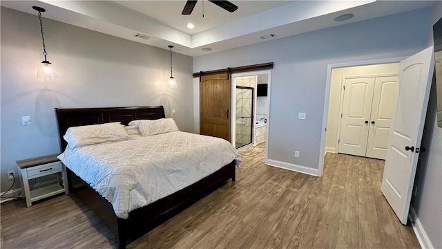 bedroom with hardwood / wood-style flooring, ceiling fan, and a barn door