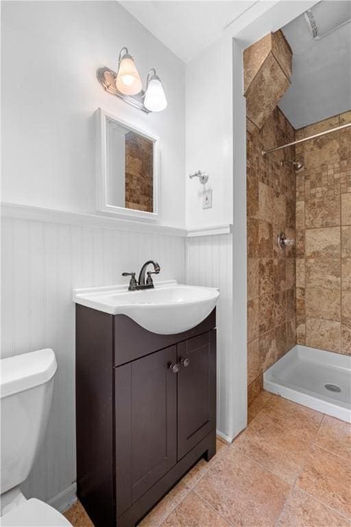 full bath with wainscoting, tiled shower, toilet, vanity, and tile patterned flooring
