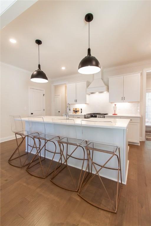 kitchen with white cabinets, a breakfast bar, custom range hood, and hanging light fixtures