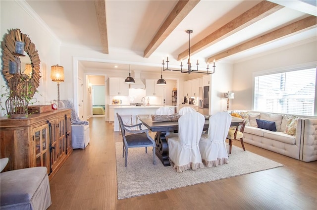 dining room with crown molding, sink, beam ceiling, light hardwood / wood-style flooring, and a chandelier