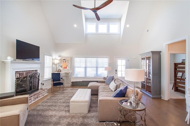 living room with hardwood / wood-style flooring, ceiling fan, a towering ceiling, and a brick fireplace