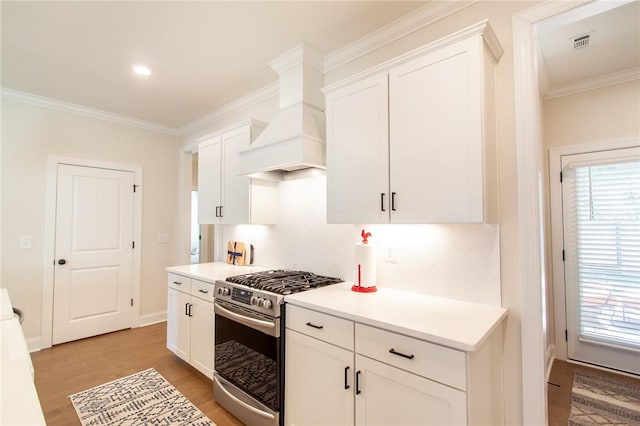 kitchen featuring stainless steel gas range oven, white cabinetry, and premium range hood