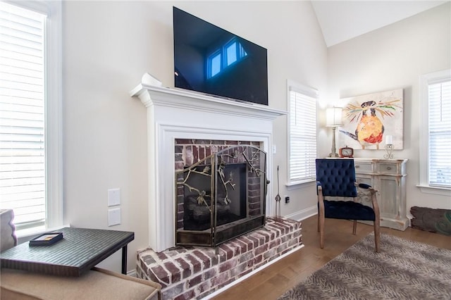 living room featuring plenty of natural light, wood-type flooring, lofted ceiling, and a brick fireplace