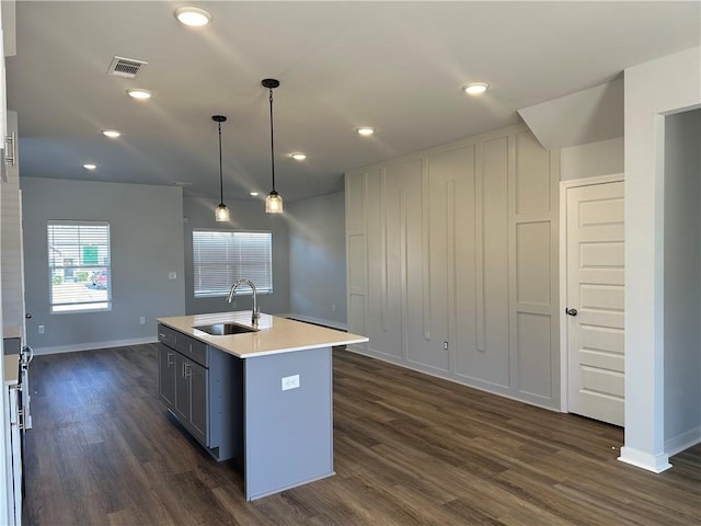 kitchen with sink, dark wood-type flooring, an island with sink, decorative light fixtures, and white cabinets