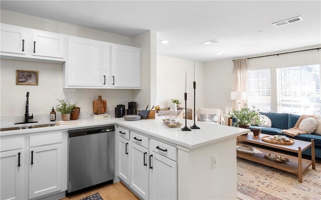 kitchen featuring stainless steel dishwasher, a peninsula, light countertops, white cabinetry, and a sink