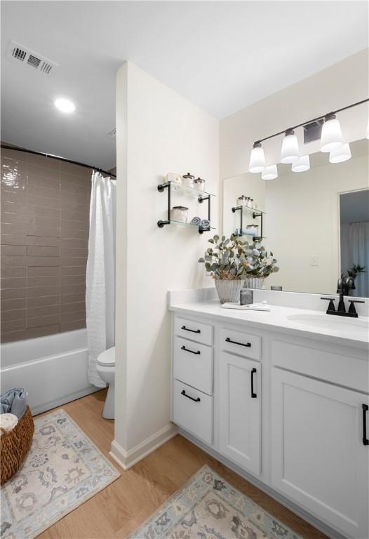 bathroom with visible vents, wood finished floors, vanity, toilet, and shower / bathtub combination with curtain