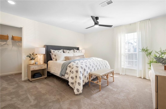 carpeted bedroom featuring visible vents, baseboards, a walk in closet, and ceiling fan
