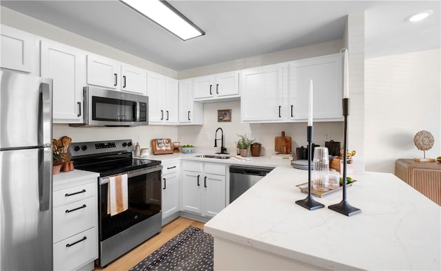 kitchen featuring white cabinets, light stone countertops, a sink, light wood finished floors, and stainless steel appliances