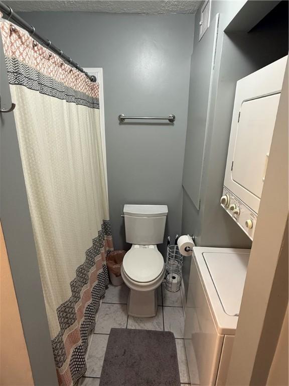 bathroom featuring toilet, tile patterned floors, a textured ceiling, a shower with curtain, and stacked washer and clothes dryer