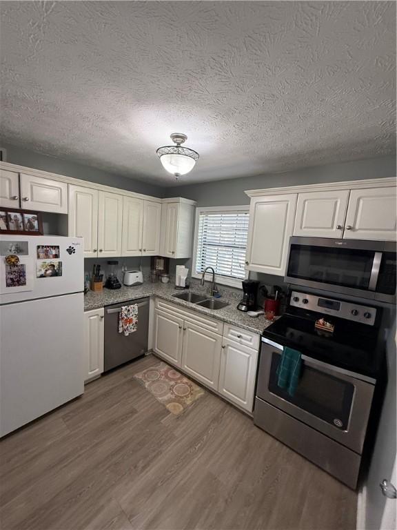 kitchen with a sink, appliances with stainless steel finishes, a textured ceiling, and white cabinetry