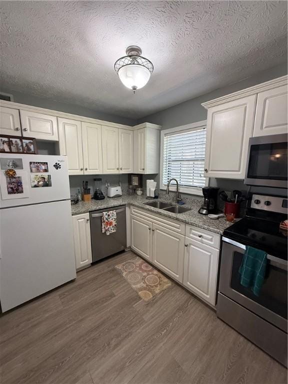 kitchen with appliances with stainless steel finishes, a sink, a textured ceiling, white cabinetry, and wood finished floors