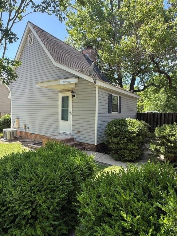 view of front of house featuring central air condition unit, roof with shingles, fence, and a chimney
