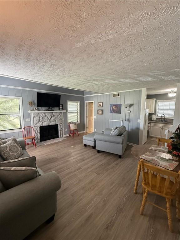 living room featuring a textured ceiling, visible vents, a stone fireplace, and wood finished floors