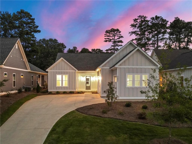 view of front of property with board and batten siding, driveway, roof with shingles, central AC, and a yard