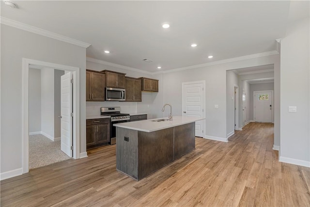 kitchen featuring a center island with sink, stainless steel appliances, crown molding, light wood-style floors, and a sink