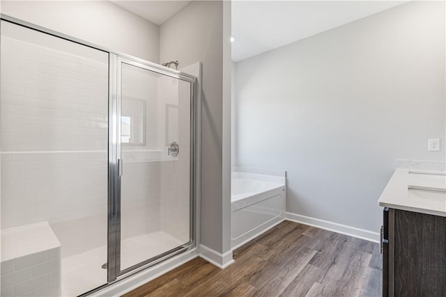 full bathroom featuring wood finished floors, baseboards, a shower stall, a bath, and double vanity