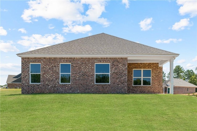 rear view of property featuring a yard, a shingled roof, and brick siding