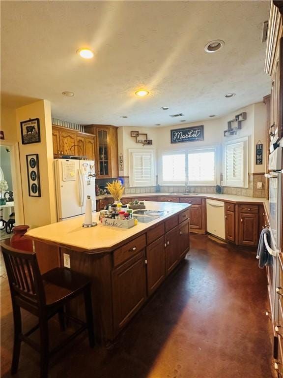 kitchen with white appliances, backsplash, sink, a kitchen island, and a kitchen bar