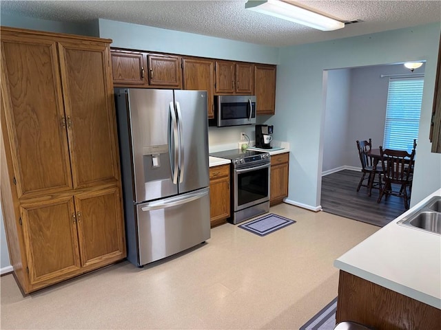 1202 Northgate Dr, Opelika, AL 36801 - kitchen with appliances with stainless steel finishes, light countertops, light flooring, a textured ceiling, and brown cabinets