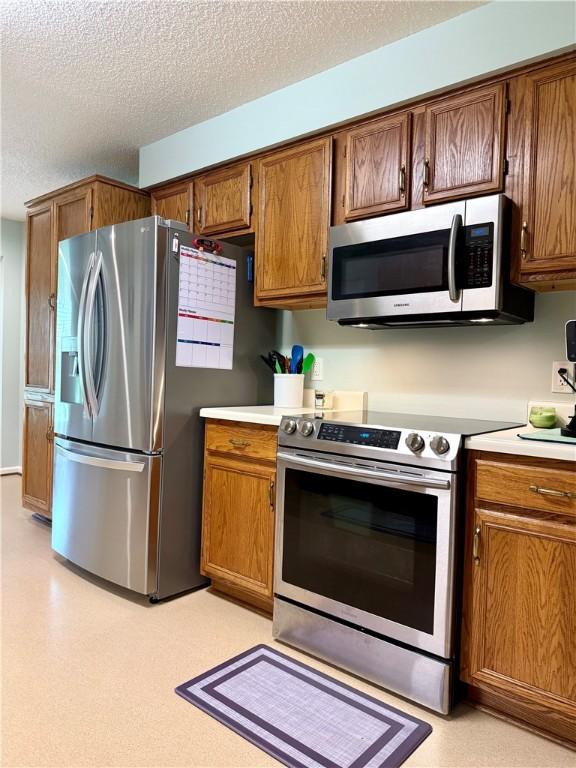1202 Northgate Dr, Opelika, AL 36801 - kitchen with stainless steel appliances, light countertops, a textured ceiling, and brown cabinetry