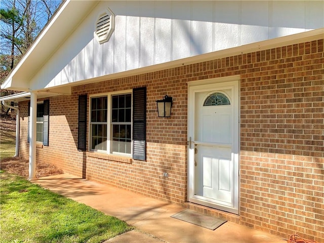 view of exterior entry featuring board and batten siding, a porch, and brick siding