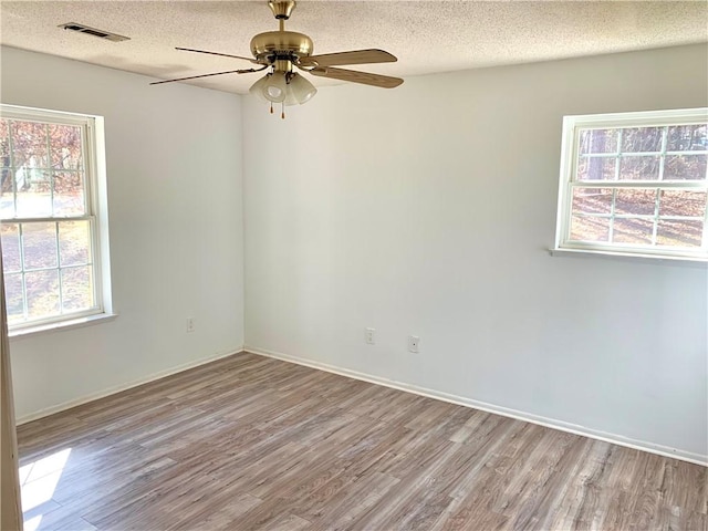 empty room featuring a ceiling fan, wood finished floors, visible vents, and a textured ceiling